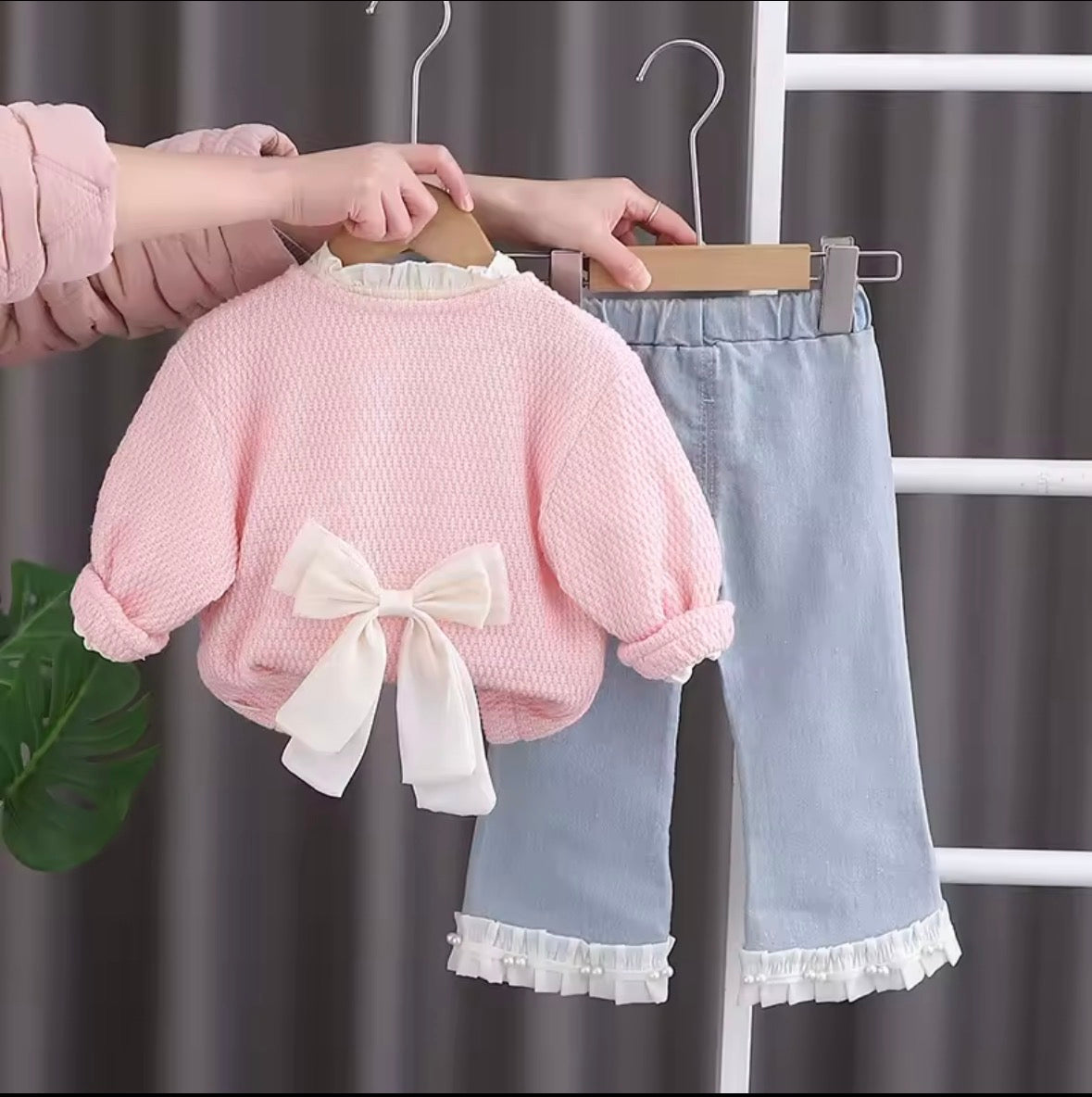 Conjunto de tres piezas , pantalón de jeans con camisa beige y abrigo (suéter) rosa con detalle de moño grande en la espalda